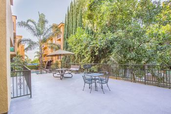 A patio with a table and chairs and trees in the background